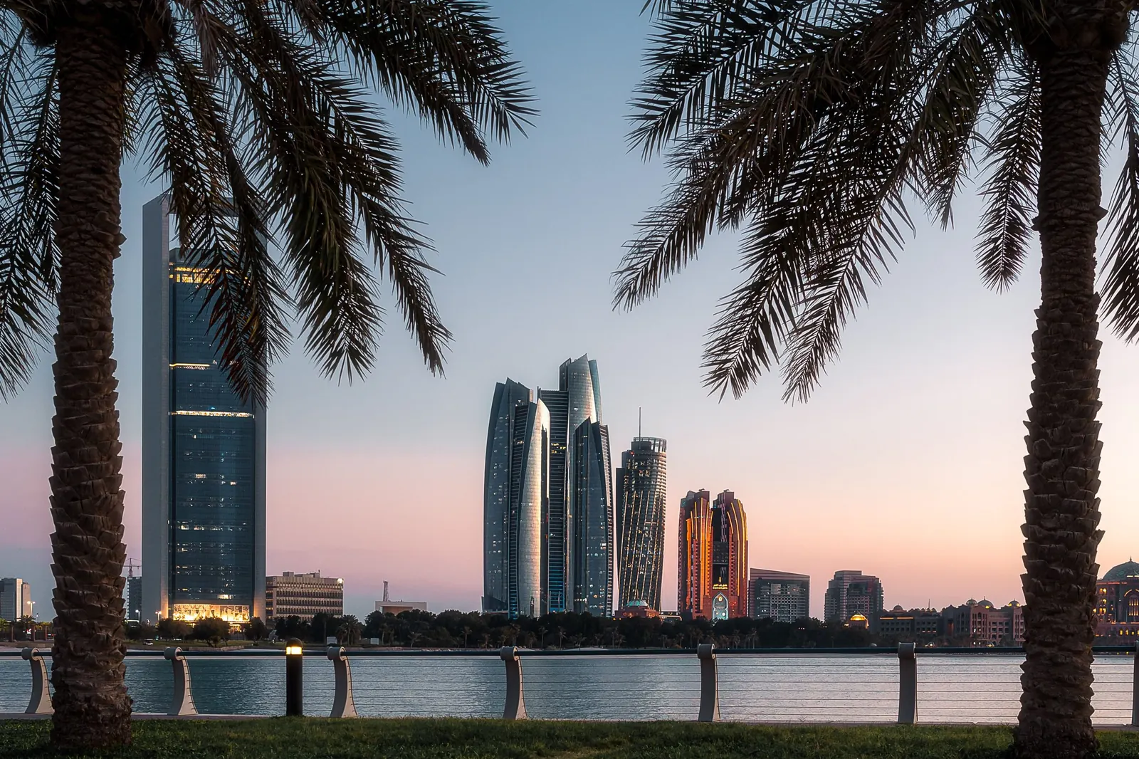 أبراج أبوظبي عند الغسق، تؤطرها أشجار النخيل على الواجهة المائية